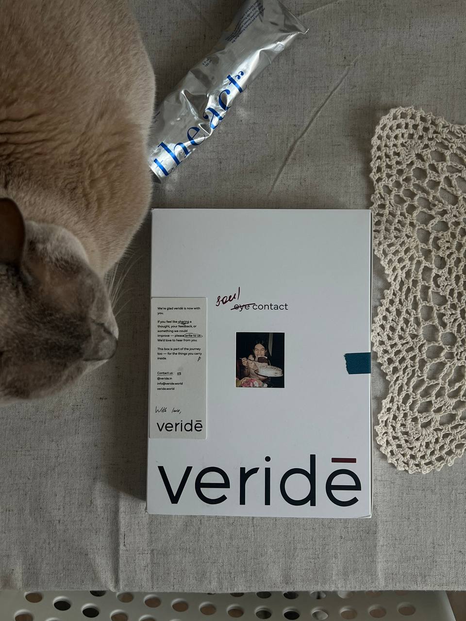 A veridē box on a linen tablecloth, photographed at home, with a cat resting beside it